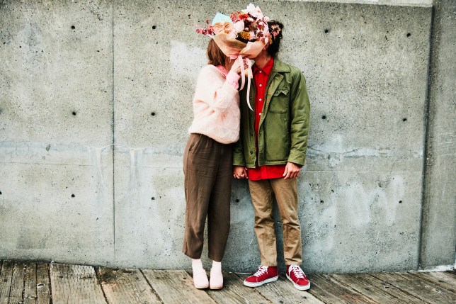 Portrait of couple kissing while hidden behind bouquet of flowers