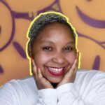 Nobuhle with her face in her hands, in front of a background of graffiti smiley faces