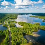 Aerial view of a winding road passing through forests & lakes in Finland on a summer day