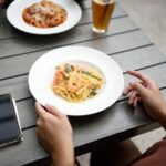 Woman's hands holding a plate of pasta on a restaurant table