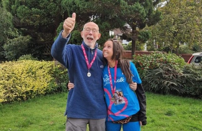 Chloe standing with her dad in the garden, their arms around each other. She's looking at him and smiling, he's looking to camera with his thumbs up