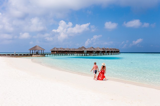 A couple walk along a white sand beach in the Maldives