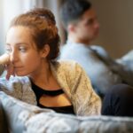 A couple sat on the sofa, woman looking unhappy/stressed