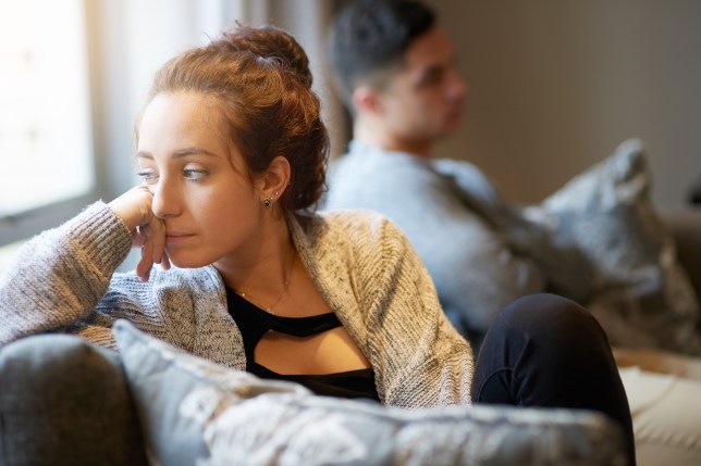 A couple sat on the sofa, woman looking unhappy/stressed