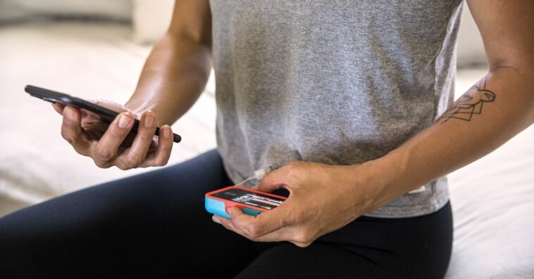 Unrecognizable woman with type-1 diabetes holds her smartphone in one hand and insulin pump in the other.