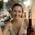 Lara at a restaurant, smiling and holding a glass of red wine