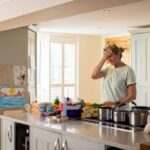 Waist-up shot of a mature female adult holding her head in disappointment in her kitchen. She has forgotten the ingredients for the Thanksgiving meal she is about t prepare. There are numerous vegetables and cooking pans on top of the kitchen island.