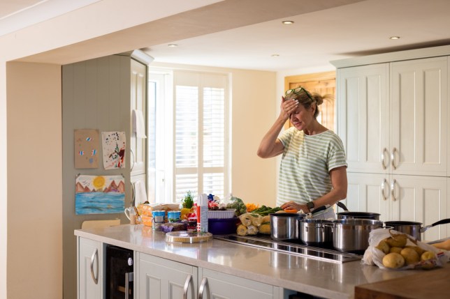 Waist-up shot of a mature female adult holding her head in disappointment in her kitchen. She has forgotten the ingredients for the Thanksgiving meal she is about t prepare. There are numerous vegetables and cooking pans on top of the kitchen island.