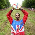 GLOUCESTER, ENGLAND - JUNE 05: Chris Anderson poses for a photo with the cheese after winning the first man's downhill race on June 05, 2022 in Gloucester, England. The Cooper's Hill Cheese-Rolling and Wake annual event returns this year after a break during the Covid pandemic. It is held on the Spring Bank Holiday at Cooper's Hill, near Gloucester and this year it happens to coincide with the Queen's Platinum Jubilee. Participants race down the 200-yard-long hill after a 3.6kg round of Double Gloucester cheese. (Photo by Cameron Smith/Getty Images)