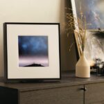 Samsung’s Music Frame speaker sitting on a brown cabinet beside a pair of cameras and some plants.