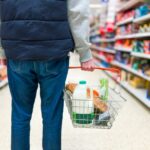 Man holding shopping basket with bread and milk groceries in supermarket