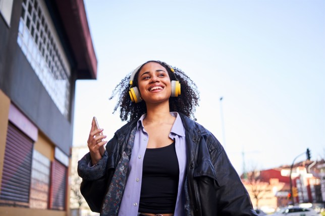 Cheerful young woman listening to music with a mobile in the street