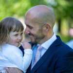 Ryan in a suit, holding his daughter - both are smiling