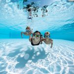 Three happy kids swimming underwater in pool