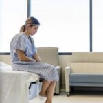 Anxious, sad, young woman wearing hospital gown looks down