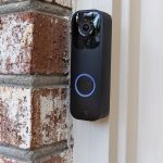 The black Blink Video Doorbell hung up on a brick wall outside of a house.