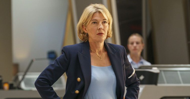 A woman standing with her hands on her hips in the center of a control room.