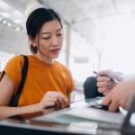 Young Asian woman travelling by airplane and doing check-in at airline check-in counter at airport terminal