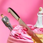 Wedding cake cut in half with bride and groom topper looking unhappy on pink background