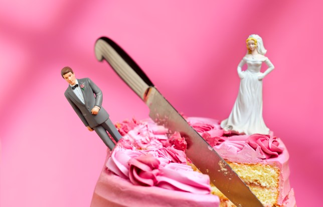 Wedding cake cut in half with bride and groom topper looking unhappy on pink background