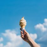 Cropped shot of woman's hand holding ice-cream cone against beautiful blue sky. It's summer! Beach holiday and vacation concept