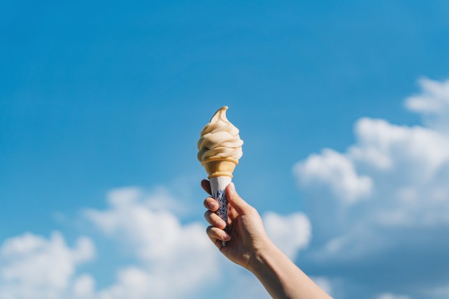 Cropped shot of woman's hand holding ice-cream cone against beautiful blue sky. It's summer! Beach holiday and vacation concept