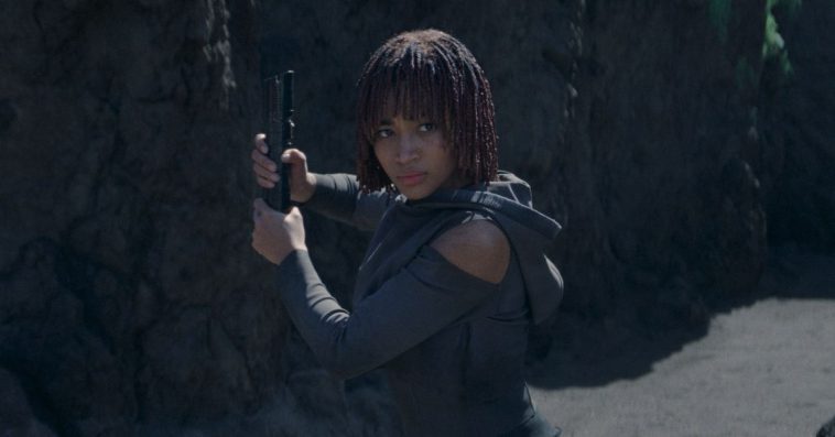 A girl wearing a gray hoodie with exposed shoulders and holding the hilt of a lightsaber as she readies for battle.