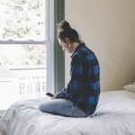 Young woman sitting on bed looking at smart phone