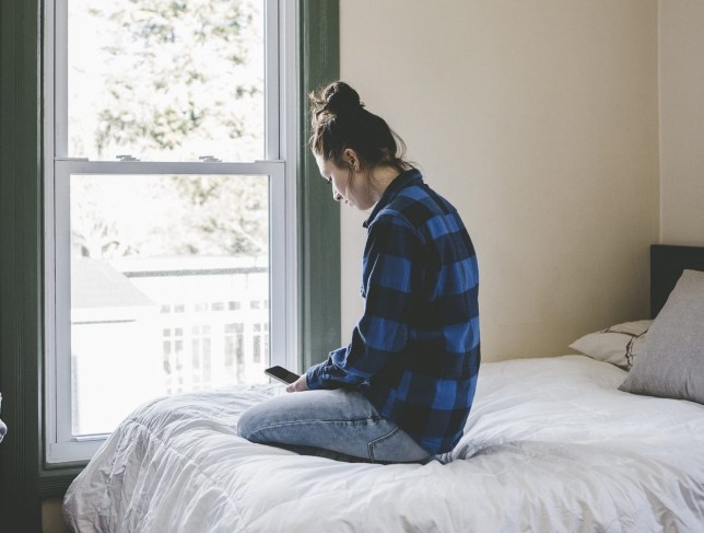 Young woman sitting on bed looking at smart phone