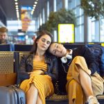 Two young women traveling by plane, waiting for flight and napping in an airport departure area.