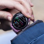 A close-up image of a pink Garmin Forerunner 265S on a woman’s wrist, just outside a blue raincoat.