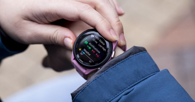 A close-up image of a pink Garmin Forerunner 265S on a woman’s wrist, just outside a blue raincoat.