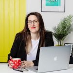 Rebecca sitting at her laptop, wearing hexagon framed black glasses