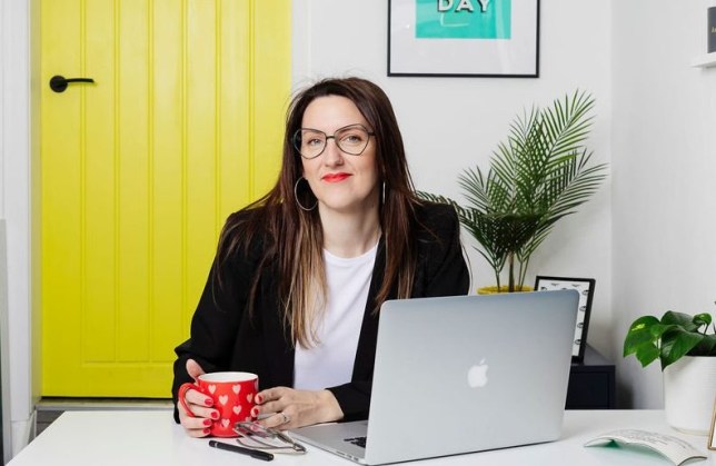 Rebecca sitting at her laptop, wearing hexagon framed black glasses