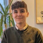 Niall Hignett inside, next to a house plant by the window