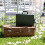 Two vintage suitcases waiting on the grass in front of wedding ceremony chairs