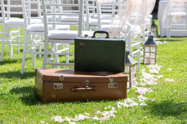 Two vintage suitcases waiting on the grass in front of wedding ceremony chairs