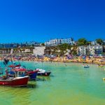 Boats in a harbour as tourists sit on the beach in Viking Bay, Kent