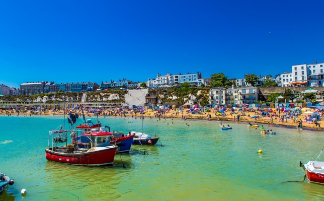 Boats in a harbour as tourists sit on the beach in Viking Bay, Kent