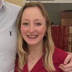 Emily Allen smiling by a bookshelf