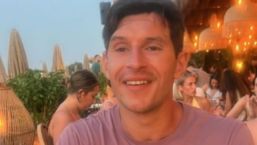 Marlon sitting at a bar, smiling - he has brown hair andtattoos on his arms