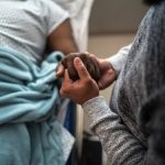 Son holding father's hand at the hospital