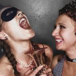 Two women laughing at a party - one is wearing an eye mask