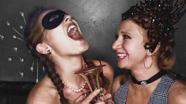 Two women laughing at a party - one is wearing an eye mask