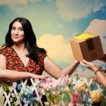 Vrinda Guha, who started taking Wegovy through a private company, takes a cardboard parcel over a floral fence. She wears a black and red floral dress