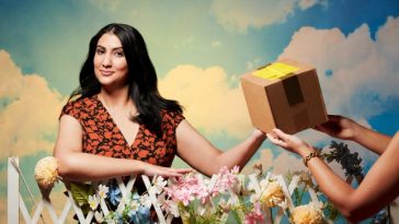 Vrinda Guha, who started taking Wegovy through a private company, takes a cardboard parcel over a floral fence. She wears a black and red floral dress