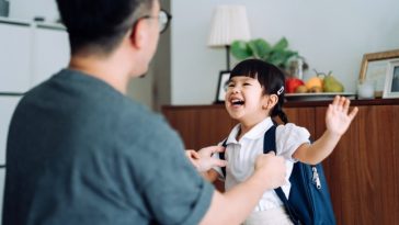 Excited and happy school girl getting dressed with her father in the living room and preparing for her first day at school