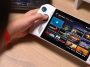 The white gamepad button-equipped seven-inch handheld gaming PC with a screen flanked on either side by joysticks, buttons, and a D-pad. Another black handheld gaming PC with a similar configuration is behind it.