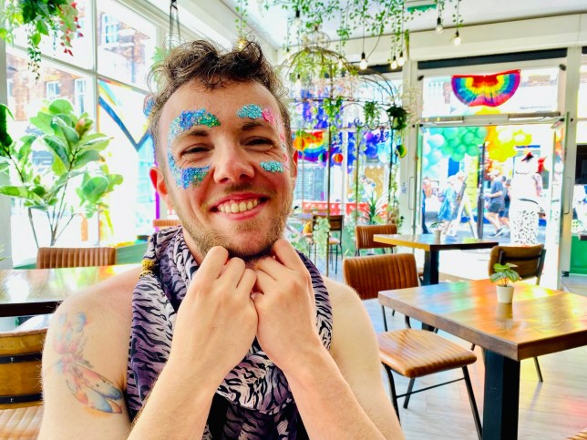 William sitting in a cafe and has glitter on their face - they are smiling happily to camera