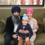 Karen sitting on a green sofa with her husband and their son on her lap - all three dressed up in suits, a dress and turbans.